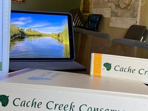 Computer monitor surrounded by policy binders for Cache Creek Conservncy