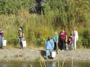 a group of people along the creek with buckets and gloves