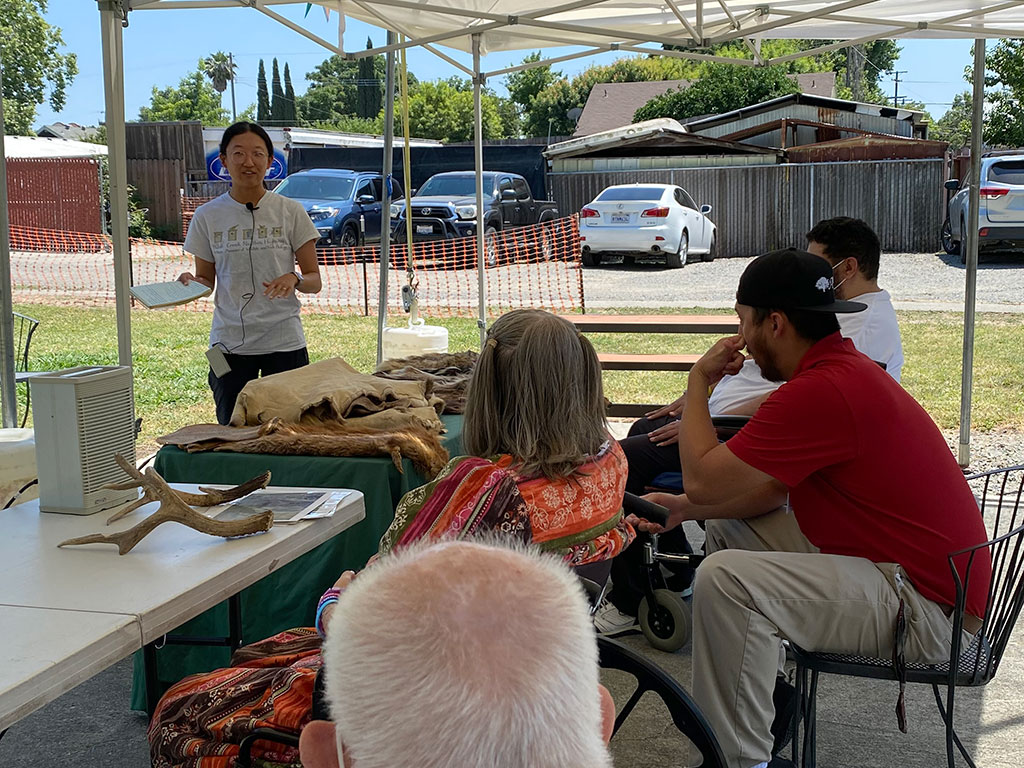 Felicia Wang, CCC Biologist standing behind a table of animal pelts, leading a discussion with a group of seated people.