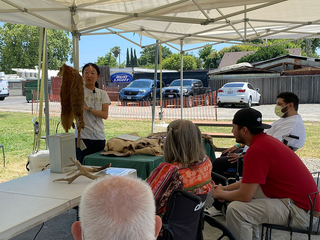 Felicia Wang, CCC Biologist holding up a beaver pelt, leading a discussion with a group of seated people.