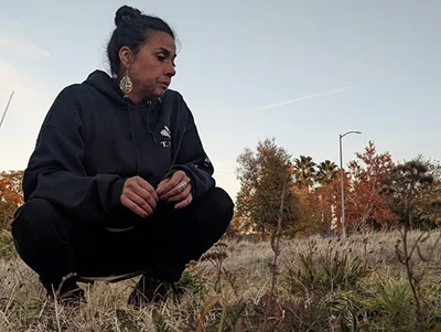 Ali Meders-Knight squatting close to the ground in a field of native grasses