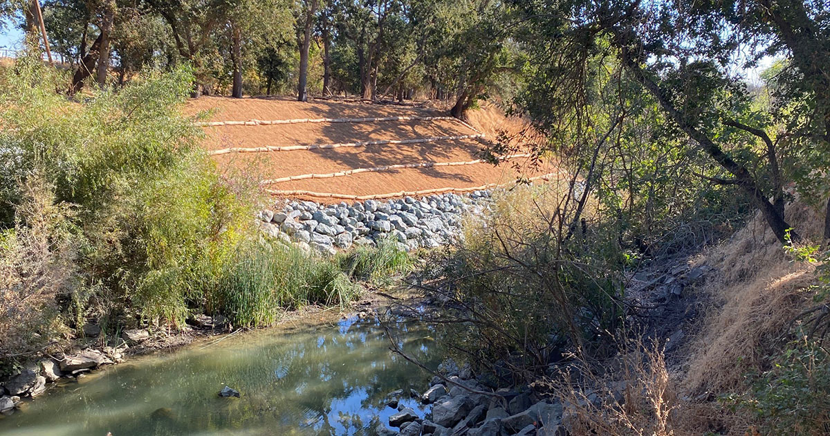 Sandbags and riprap on slope across a shallow creek