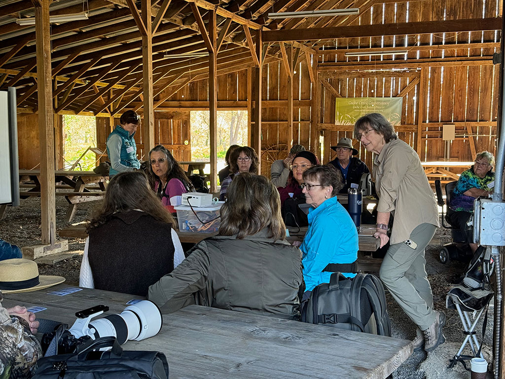 Jan Lightfoot and several people sitting at picnic benches in the old, wood barn at the Nature Preserve