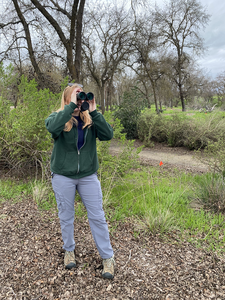 Woman in a Riparian forest looking thru binoculars
