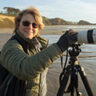 Jan Lightfoot looking at camera on a beach with camera on tripod