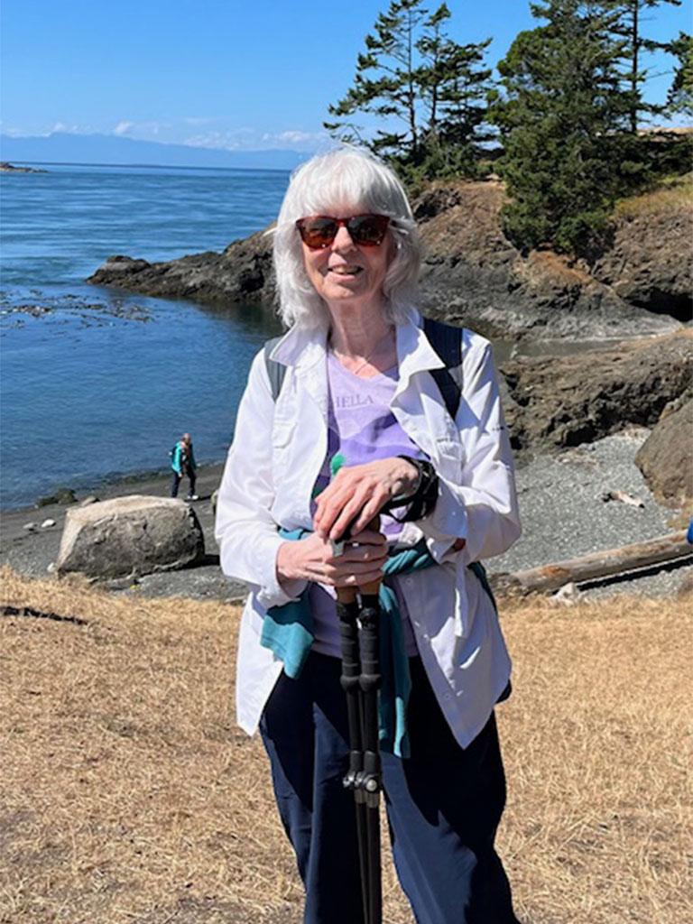 Woman with white hair holding a camera with the ocean in the background