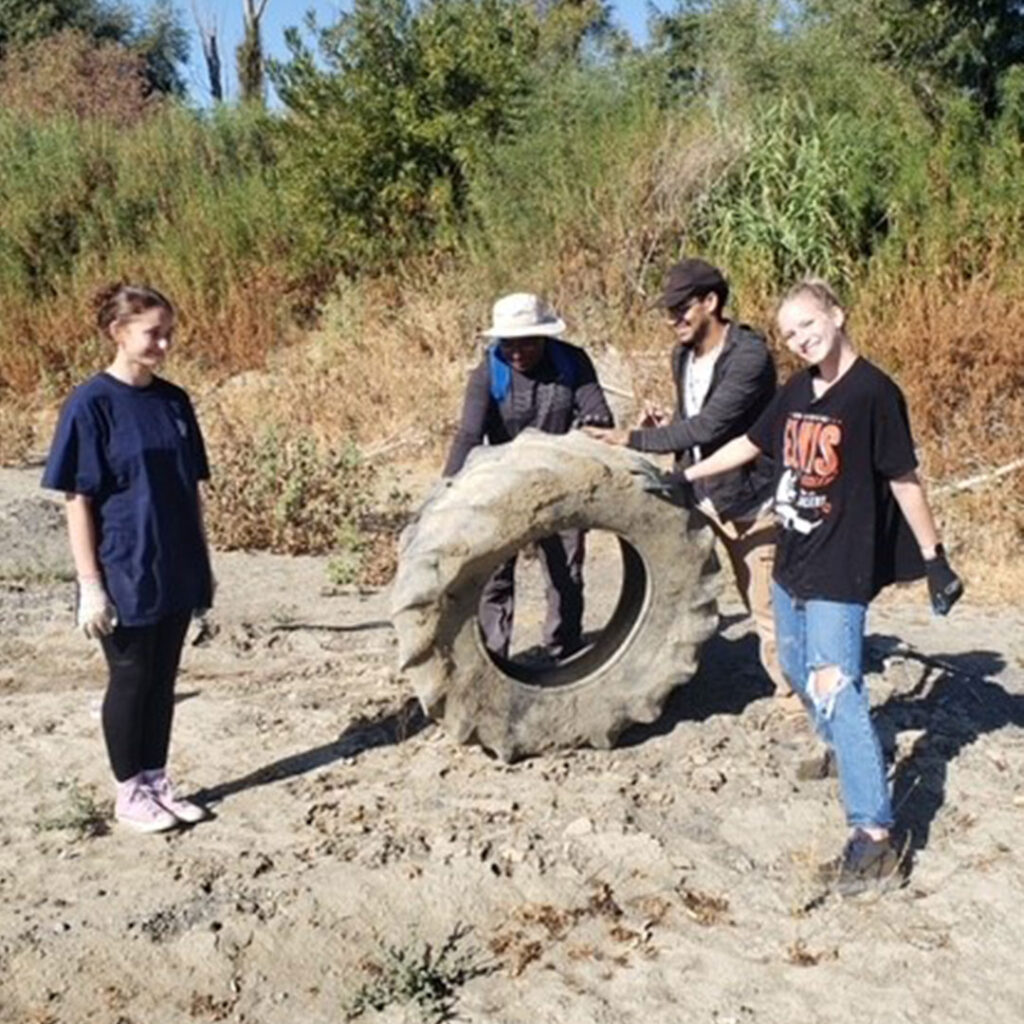 Four young people with a large, dirty tractor tire dug up from the creek bed