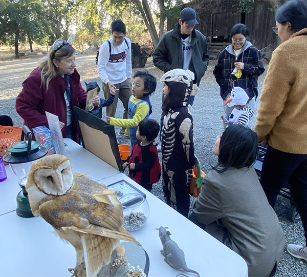 Children in Halloween costumes near table with an Owl and a rat and more talking to Nancy Ullrey surrounded by adults and older kids