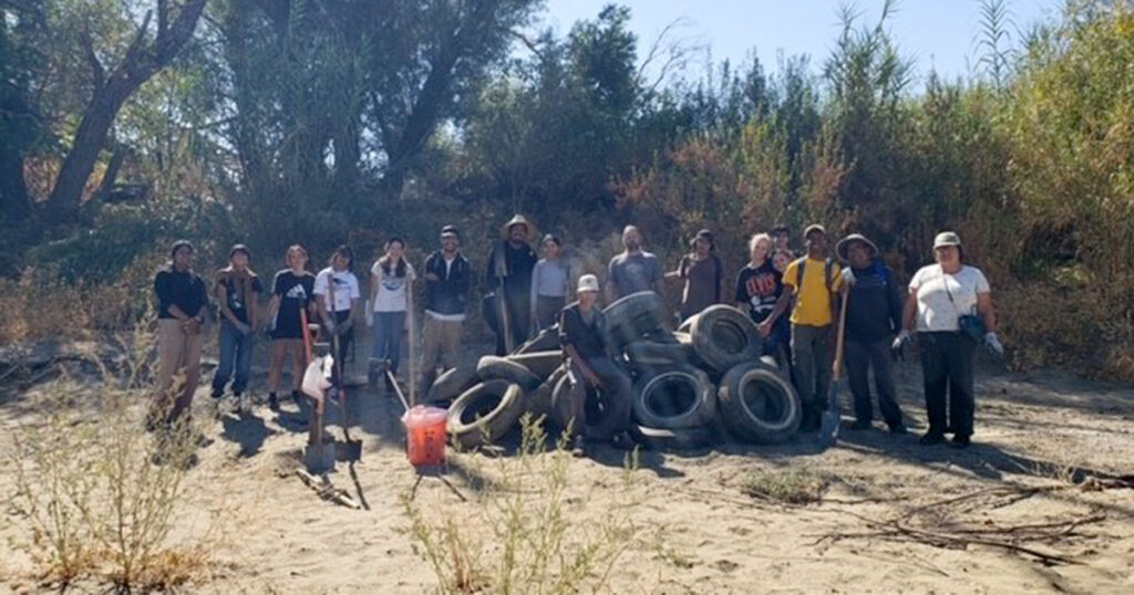 Several people standing in a dry creek bed behind a pile of tires they dug up