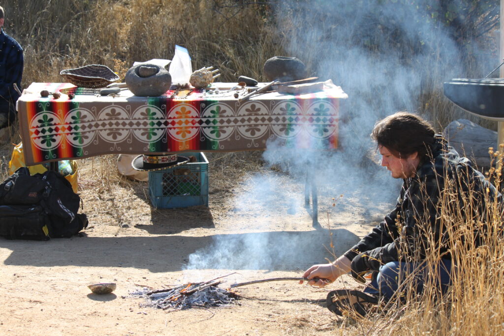 Image of table with cultural objects on it next to a small fire being tended to by a student